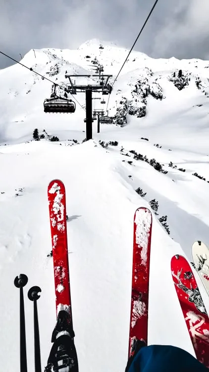 Skis and poles pointing downhill toward a snowy mountain and chairlift.