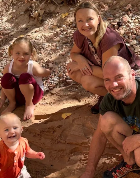 Trent and Christina Owen with their two children, Aspen and Jasper, sitting together outdoors on red rock and sand.