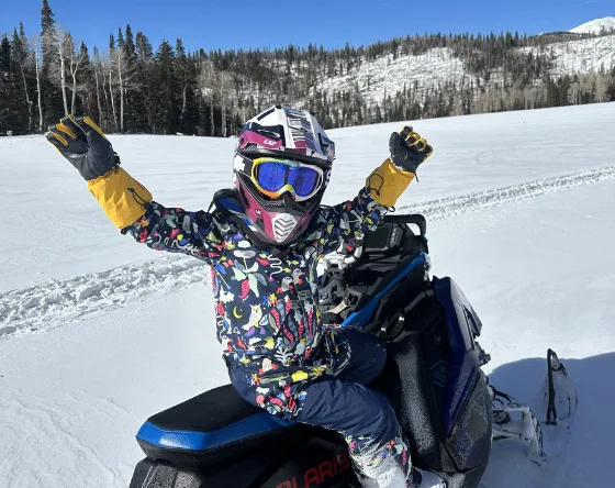 One of the Owen children in a helmet and goggles riding a snowmobile across a snowy meadow near Eagle Point.