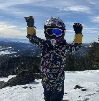 One of the Owen children in winter gear raising both arms on a snowy overlook above the mountain valleys near Eagle Point.